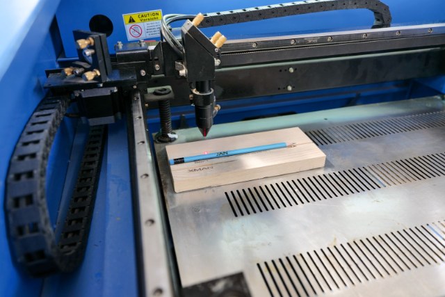CO2 laser engraver working on a wood board on the machine bed